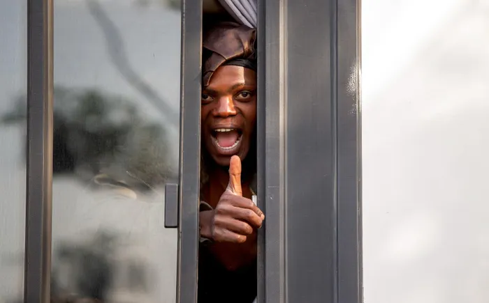 A foreign national gives a thumbs-up from inside a bus at Durban’s Old Drive-In site as repatriation transport operations continue under coordinated processing and security monitoring.
