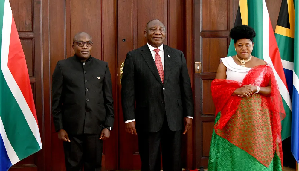 Two men in black suits next to a woman in green skirt and white top