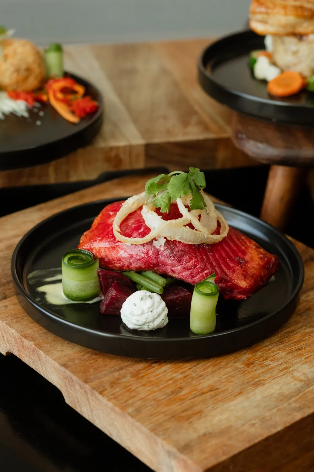Food dish, salmon infused with beetroot, on a black plate with blue cheese cream and homemade pickle.