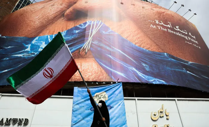 A woman waves an Iranian flag in front of an anti-US billboard referring to US President Donald Trump and the Strait of Hormuz at Valiasr Square in Tehran.