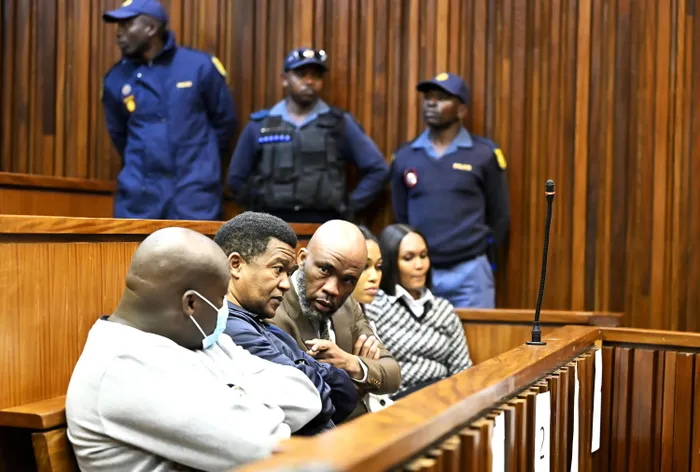 Vusimuzi 'Cat' Matlala leans in to speak with a co-accused in the dock, flanked by his fellow accused and under police guard, during their trial in the Johannesburg High Court