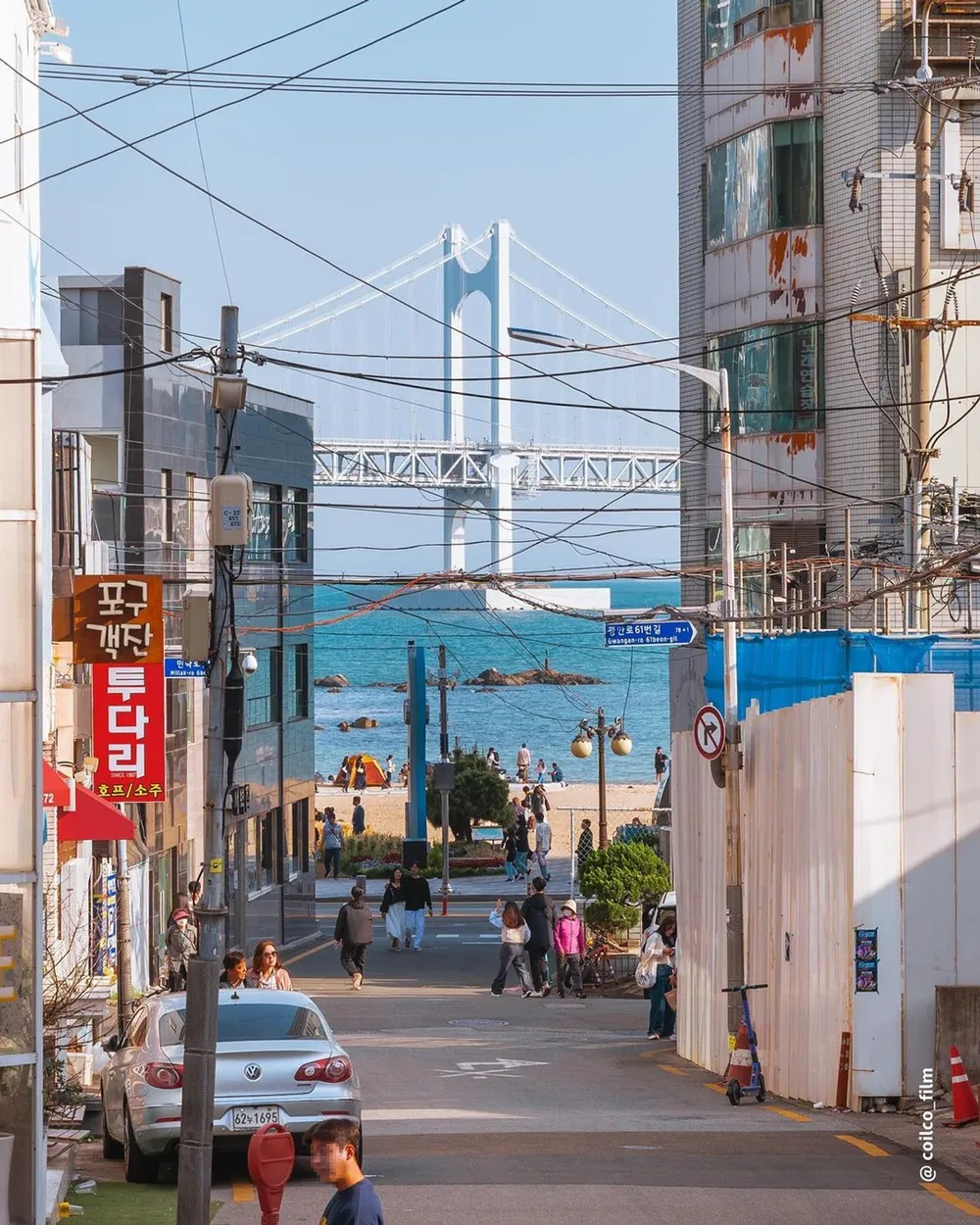 A glimpse of see at the end of narrow road lined with colourful signs.