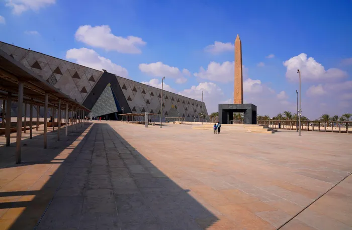 Clear skies frame a wide-angle view of the Grand Egyptian Museum, highlighting a prominent obelisk.