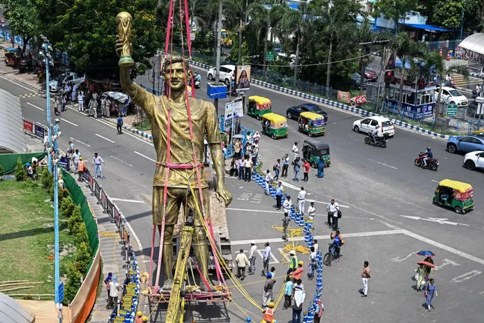 Pedestrians watch as workers remove a statue of Argentine football player Lionel Messi for its re-installation to a safer place in Kolkata. 