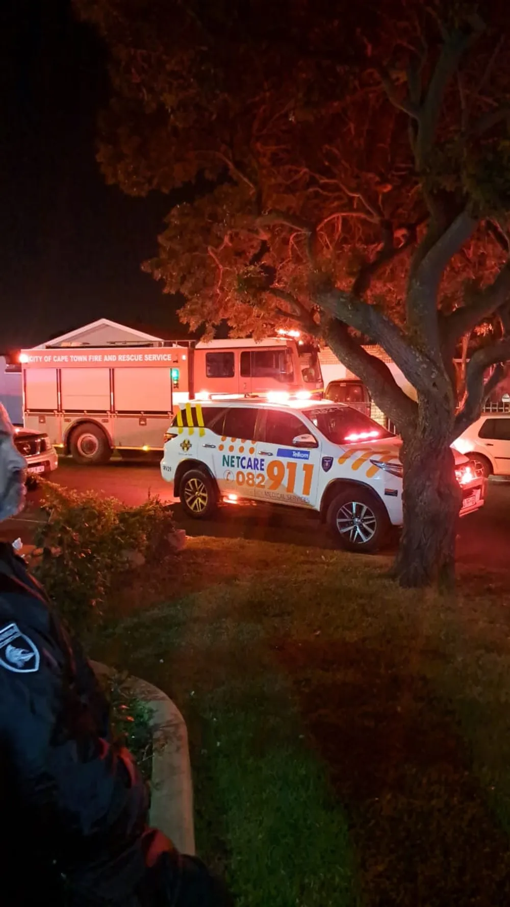 Picture of emergency vehicles, lights on, parked in the street at night.