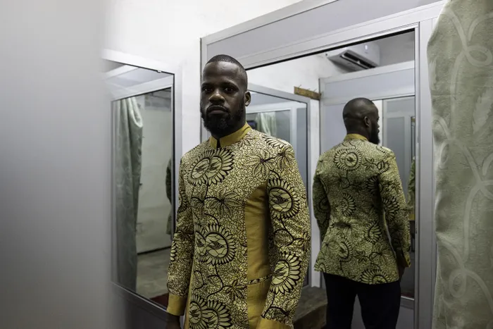 Auguy Okasol poses for a photo wearing a "abacost", a closed-front jacket, at the Okasol workshop in Kinshasa. Sewing machines whirred across bold fabrics at a Kinshasa atelier where Congolese tailors and their style-savvy customers have revived a suit long associated with life under a dictator.
