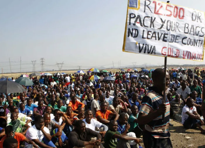 FED UP: A miner holds a placard as strikers gather at Lonmin's Marikana mine. The excesses of the government are another reason why people at the bottom are forced to protest, says the writer. Picture: Reuters
