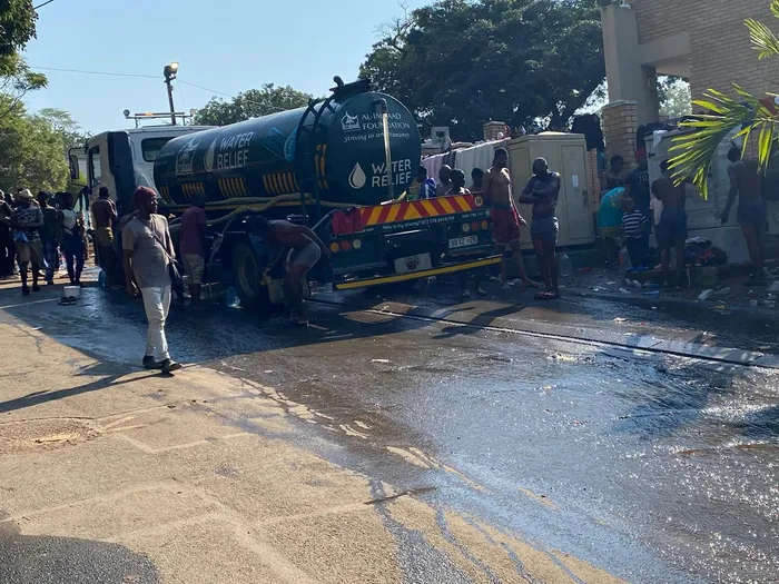 Local residents in Sherwood express growing concerns over the influx of over 10,000 foreign nationals camping outside their community hall, highlighting issues of hygiene, safety, and the impact on their neighborhood. In Picture: Male Foreign Nationals taking a bath by the water truck in Sherwood. 