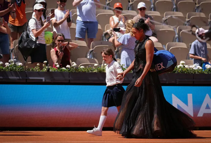 Japan's Naomi Osaka holds a mascots hand as she walks on Court Suzanne-Lenglen to player her women's singles match against Germany's Laura Siegemund.
