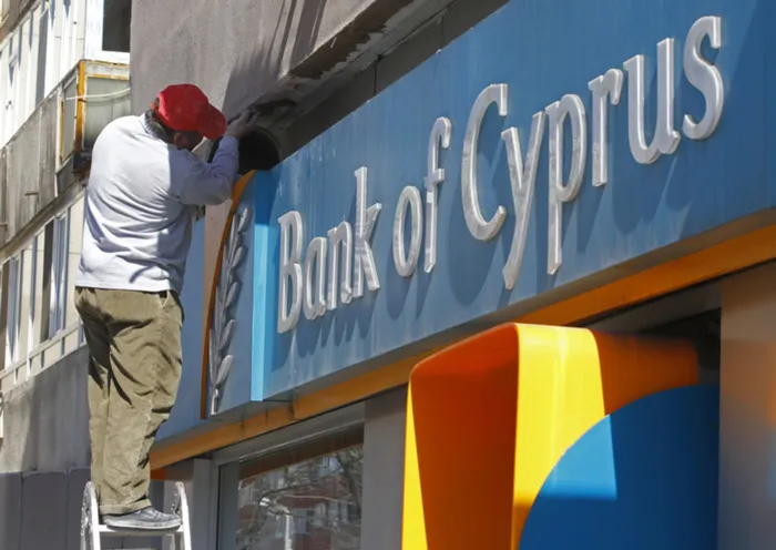 A worker paints a wall above a branch of Bank of Cyprus.