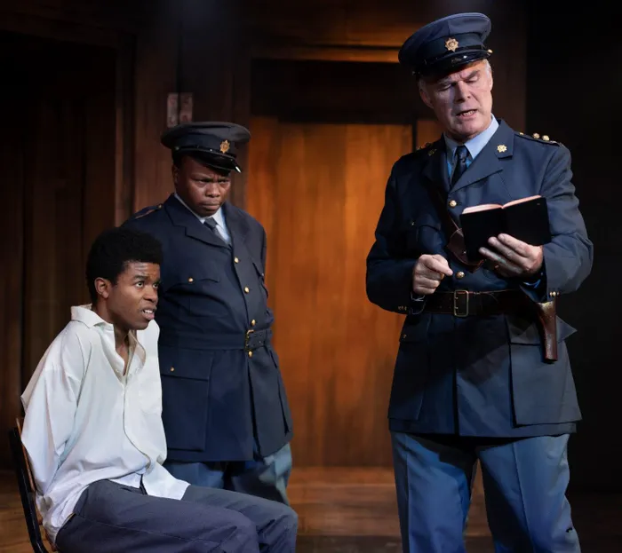 A tense interrogation scene featuring Alex Sono (playing student leader Bafana Buthelezi), alongside Sbuja Dywili and Deon Lotz portraying apartheid-era police officers.