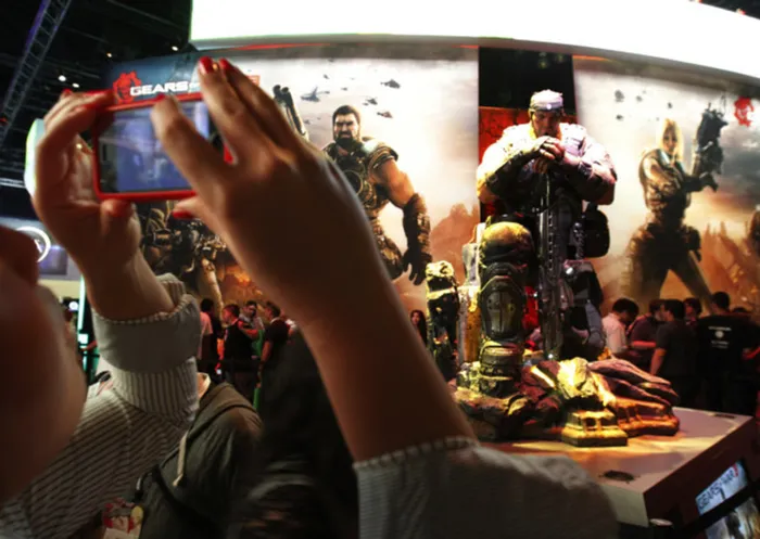 A woman photographs the Gears of War 3 game display at E3 in Los Angeles.