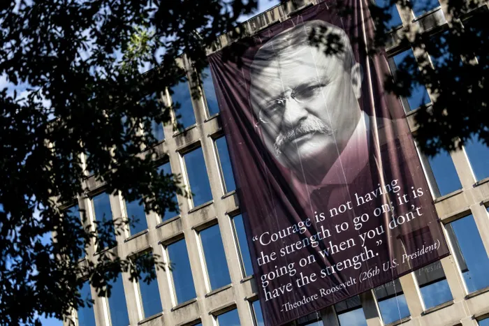 A banner says, “Courage is not having the strength to go on; it is going on when you don’t have the strength,” with a portrait of Theodore Roosevelt, outside the Theodore Roosevelt Federal Building in D.C.
