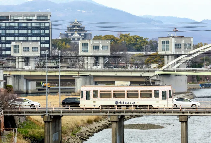 An “Okaden” tram crosses the Asahi River with Okayama Castle in the background.