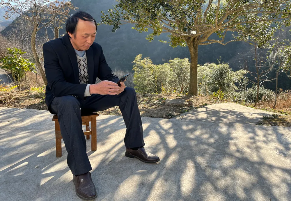 Photo taken on Dec. 5, 2021, shows Liu Wenguo scrolling through his phone in the yard at the front of the family's house. (People's Daily Online/Meng Bin)