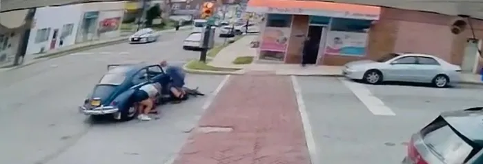Surveillance footage shows the Volkswagen Beetle driver and a local business owner trying to lift the car before more help arrived.