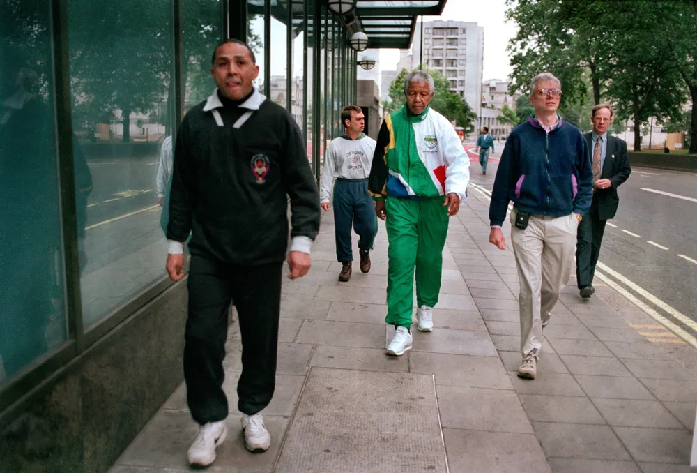 South African President Nelson Mandela takes a 6 am walking along Park Lane, accompanied by his bodyguards, during a visit to London, July 1996. He is wearing a track suit in the South African national colours, with the Olympic logo on them