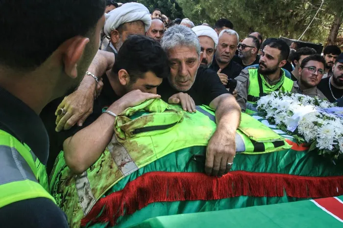 Men mourn over a coffin wrapped in the Amal Movement flag and topped with a blood-stained civil defence vest during the funeral in Sidon on June 7, 2026, of four people killed in an Israeli airstrike the previous day in the southern village of Zibdin.