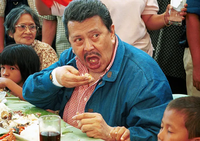 Philippine President Joseph Estrada, center, opens his mouth wide as he eats with his hands during his 63rd birthday celebration in Taytay, Rizal province, east of Manila, Wednesday, April 19, 2000. Estrada, a former movie star who won the elections with his pro-poor program, spends his birthdays eating with poor families near their homes. (AP Photo/Aaron Favila)