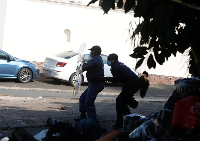 Police use a riot shield to protect themselves from objects such as rocks and bricks thrown by frustrated undocumented immigrants at the Sherwood site.