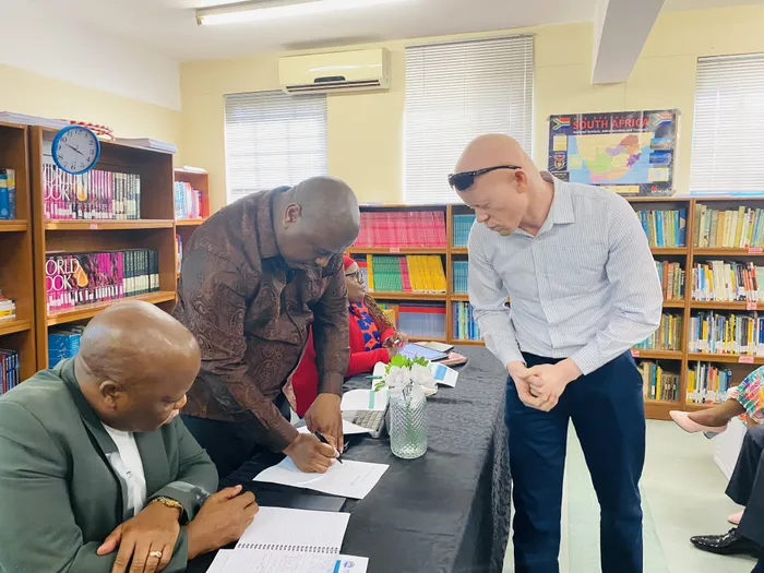 The MEC of Education in KwaZulu-Natal, Sipho Hlomuka, signs a memorandum from parents while uMkhumbane Secondary School SGB member Bulelani Majola and KZN Education Head of Department Nkosinathi Ngcobo observe.