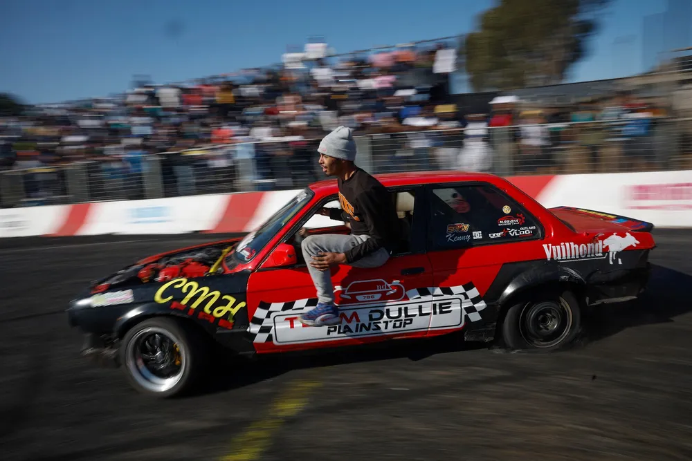 A member of Team Dullie hangs out of their car as they drift during a round of spinning at Wheelz n Smoke Arena in the south of Johannesburg.